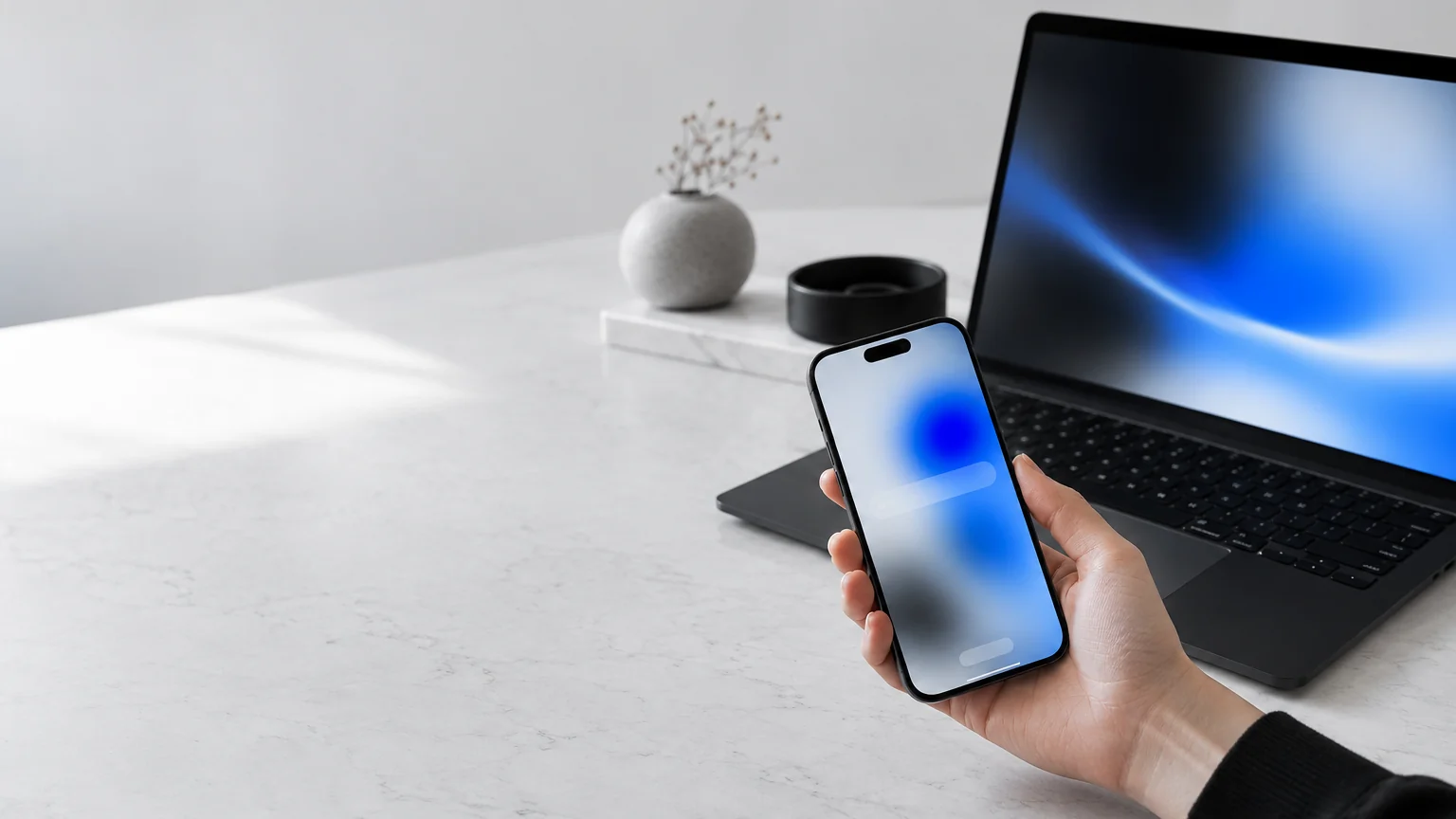 Main tenant un smartphone avec une recherche floutée devant un ordinateur portable éclairé de bleu