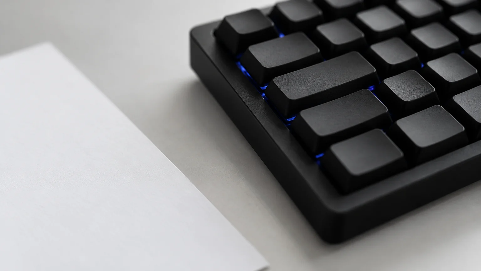 Gros plan sur un clavier noir et une feuille blanche avec un rétroéclairage bleu discret
