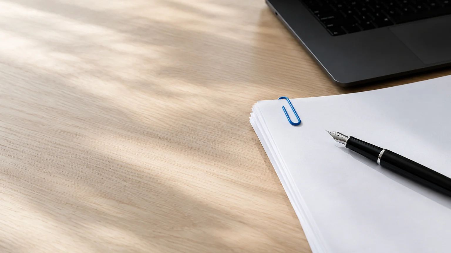 Pile de documents blancs avec un stylo et un trombone bleu sur un bureau en chêne clair
